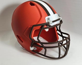 May include: An orange football helmet with a brown face mask and a white stripe down the center. The helmet has a glossy finish and is sitting on a white surface. The helmet is a replica of a professional football team's helmet.