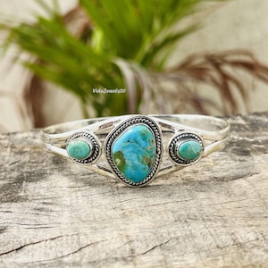 May include: A silver cuff bracelet featuring a large, central, irregular turquoise stone flanked by two smaller, oval-shaped turquoise stones. Each stone is set in a twisted silver wire border, and the metal band has a polished finish.