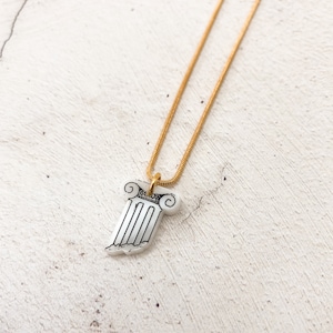 May include: A gold chain necklace with a white pendant shaped like a broken column.