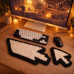 May include: A desk setup with a black and white mechanical keyboard, a black mouse, and two arrow-shaped rugs with a white centre and black border. A computer monitor and a cup of coffee are also visible.