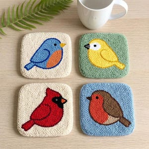May include: Set of four square coasters with embroidered bird designs. Includes a bluebird, yellow bird, red cardinal, and a robin. Each coaster features a different bird on a textured background, perfect for home decor.