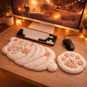 May include: A fluffy, cream-colored bear-shaped desk mat and a matching paw-shaped mousepad. The bear mat features a smiling bear face and paw pads in a soft peach color. The items are on a wooden desk with a keyboard and mouse.