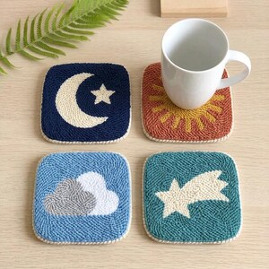 May include: Set of four square coasters with celestial and weather-themed designs. Includes a navy blue coaster with a crescent moon and star, a red-orange coaster with a sun, a light blue coaster with a cloud, and a teal coaster with a shooting star.