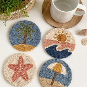 May include: Four circular punch needle coasters featuring beach-themed designs: a palm tree on sand, a sun over ocean waves, a pink starfish on a cream background, and a yellow beach umbrella on sand. Each coaster has a textured, looped yarn finish.