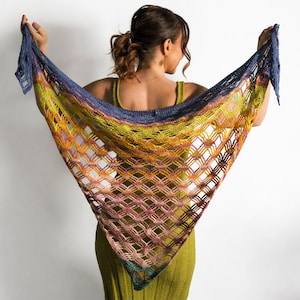 May include: A colorful, open-weave shawl in a triangular shape. The shawl features a gradient of colors, including blue, yellow, orange, and pink. The open weave creates a diamond pattern. The shawl is held up by a person.