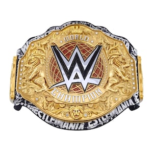 May include: A gold-colored wrestling championship belt with the WWE logo in the center. The belt features intricate detailing, including lion figures and the words "World Champion" and "WrestleMania". The background is white.