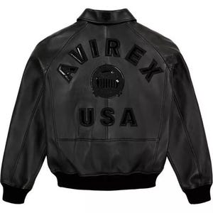 Pode incluir: Casaco de couro preto com a palavra "AVIREX" arqueada nas costas, acima de um emblema circular e da palavra "USA". O casaco tem um estilo bomber cl&aacute;ssico com gola e punhos e bainha canelados.