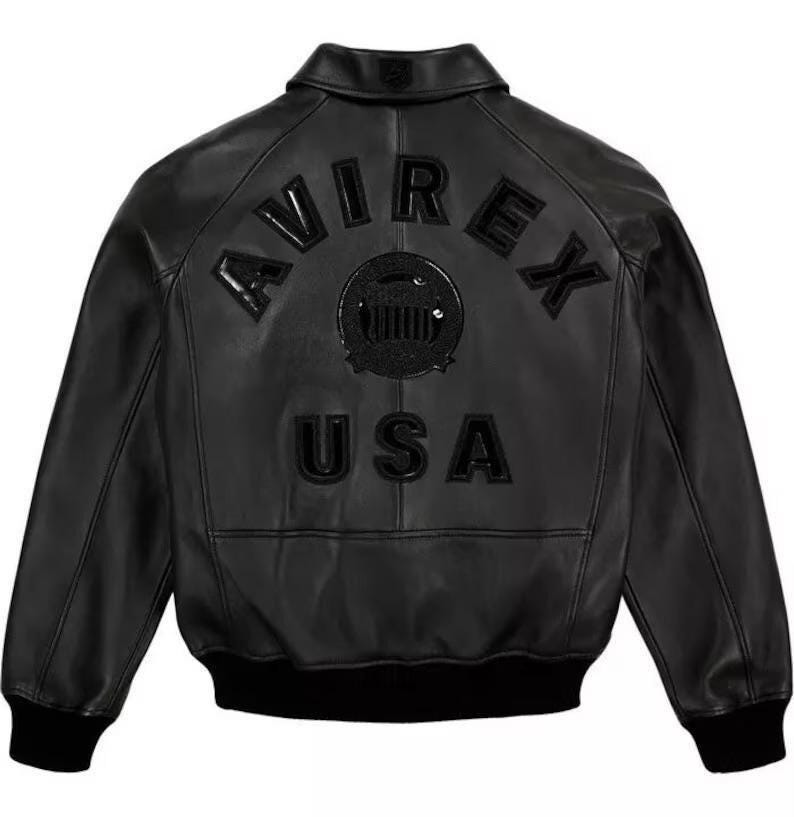 Pode incluir: Casaco de couro preto com a palavra "AVIREX" arqueada nas costas, acima de um emblema circular e da palavra "USA". O casaco tem um estilo bomber cl&aacute;ssico com gola e punhos e bainha canelados.