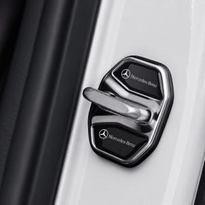 Może przedstawiać: Chromowana osłona zamka drzwi samochodu z dwoma czarnymi panelami. Każdy panel ma logo i tekst Mercedes-Benz w kolorze białym. Dźwignia blokady jest srebrna. Osłona jest zamontowana na białych drzwiach samochodu.