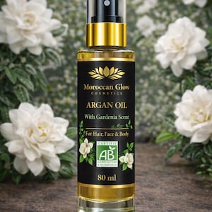 Puede incluir: Una botella de vidrio transparente de aceite de arg&aacute;n Moroccan Glow Cosmetics con aroma a gardenia. La etiqueta es negra con detalles dorados y texto blanco. La botella contiene 80 ml de aceite y es apta para cabello, rostro y cuerpo. Flores blancas en el fondo.