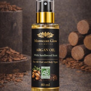 Puede incluir: Una botella de vidrio transparente de Aceite de Arg&aacute;n Moroccan Glow con tapa dorada y etiqueta negra. La etiqueta dice "ARGAN OIL With Sandalwood Scent" y "For All Hair and Body Types". La botella contiene 80 ml de producto.