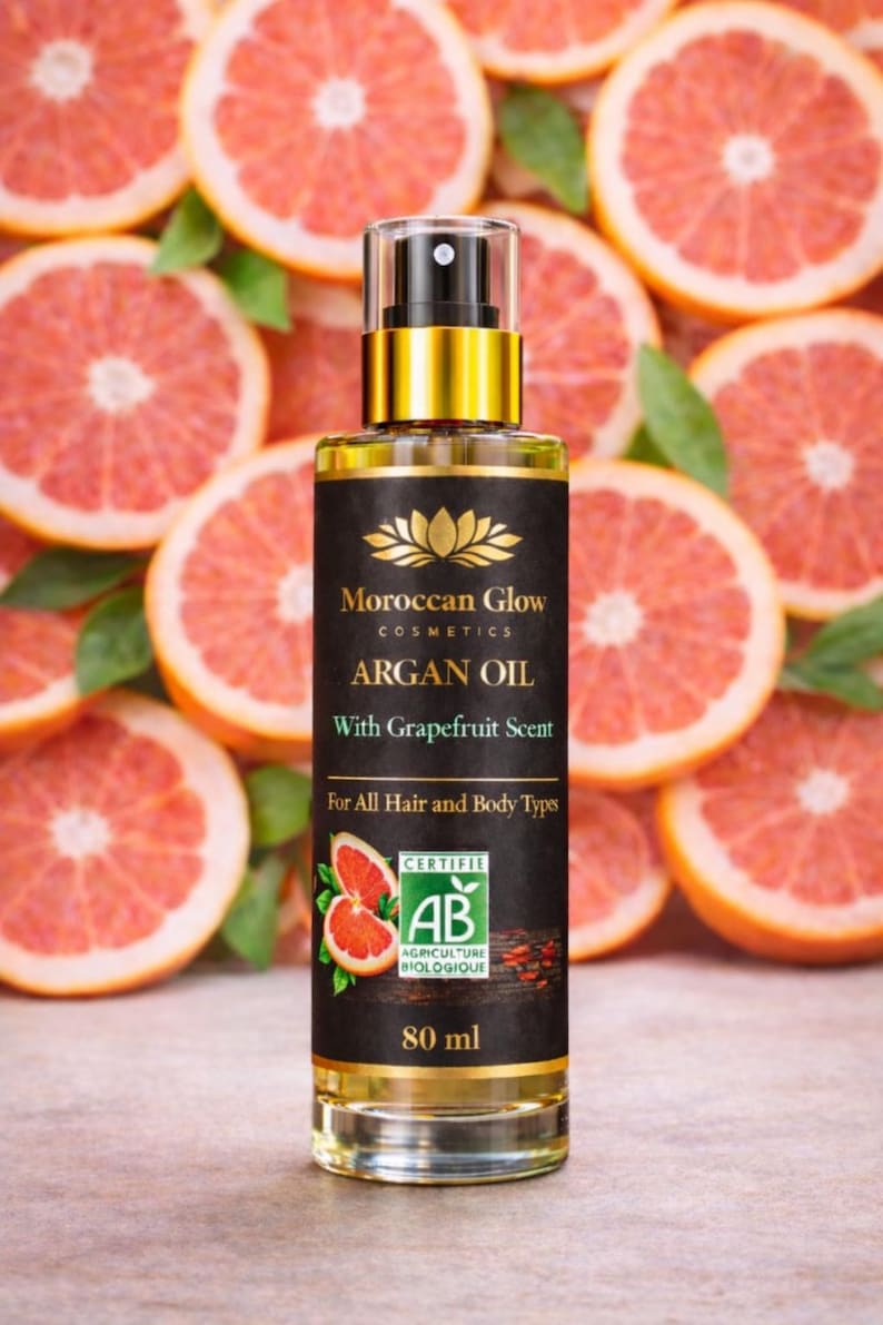 Puede incluir: Una botella de aceite de arg&aacute;n Moroccan Glow con aroma a pomelo, para cabello y cuerpo, se muestra sobre un fondo de rodajas de pomelo. La botella es de 80 ml y tiene una etiqueta dorada y negra con la certificaci&oacute;n AB Agriculture Biologique.