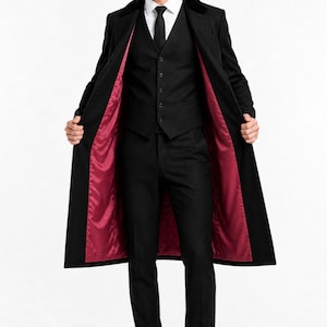 Puede incluir: Un traje negro con un abrigo largo, chaleco y pantalón. El abrigo tiene un forro rojo. El atuendo incluye una corbata negra, camisa blanca y gorra negra. La persona lleva zapatos negros.