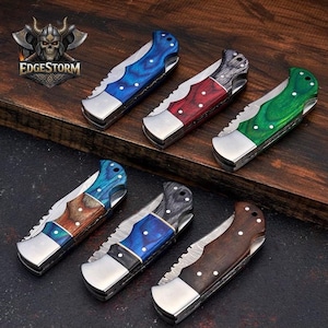 May include: Six folding pocket knives with metallic bolsters and handles in various finishes, including blue, red, green, and natural wood grain patterns. Each knife features a serrated spine section and three visible rivets on the handle scales.