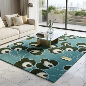 Puede incluir: Una alfombra rectangular con un diseño floral en tonos turquesa, verde y blanco. La alfombra está en un salón con un sofá, una mesa de centro y grandes ventanales. Las dimensiones de la alfombra no son visibles.