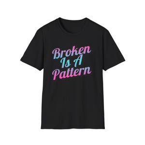 Könnte beinhalten: Schwarzes T-Shirt mit dem Schriftzug "Broken Is A Pattern" in einem Farbverlauf aus Rosa und Blau. Der Text ist in einer Schreibschrift gehalten. Das T-Shirt hat kurze Ärmel und einen Rundhalsausschnitt.
