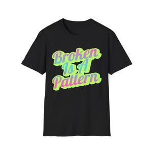 May include: Black t-shirt with the text "Broken Is A Pattern" in a colourful, stylised font. The text features a gradient of blue, green, and pink. The shirt is a classic crew neck style.