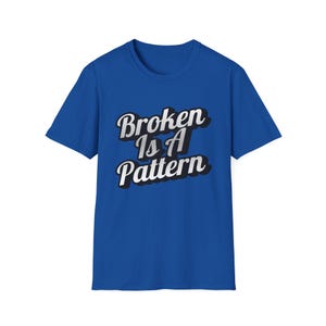 May include: A royal blue t-shirt featuring the text "Broken Is A Pattern". The text is in a layered font, with white and black shadowing for a 3D effect. The shirt has a crew neck and short sleeves. The design is centered on the chest.