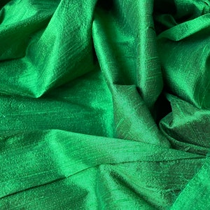 Può includere: Primo piano di un tessuto verde liscio con un leggero luccichio. Il tessuto è drappeggiato e piegato, creando linee morbide e fluide.