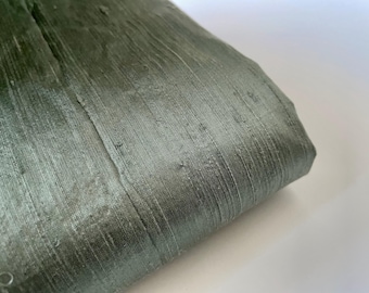 May include: A close-up of a piece of green silk fabric with a subtle sheen. The fabric has a smooth, luxurious texture.