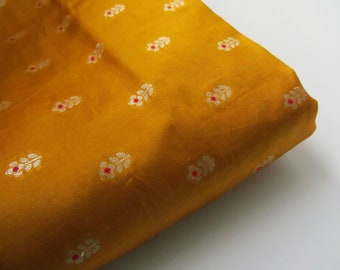 Könnte beinhalten: Ein Nahaufnahme eines senfgelben Stoffes mit einem sich wiederholenden Muster aus kleinen weißen und roten Blüten.