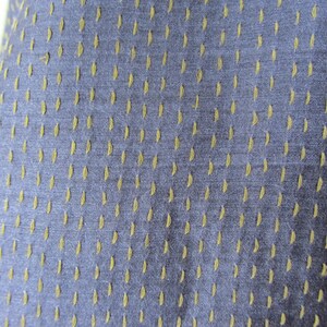 Peut inclure: Gros plan sur un tissu bleu avec un motif subtil de petits points vert clair. Le tissu a une apparence textur&eacute;e et tiss&eacute;e.