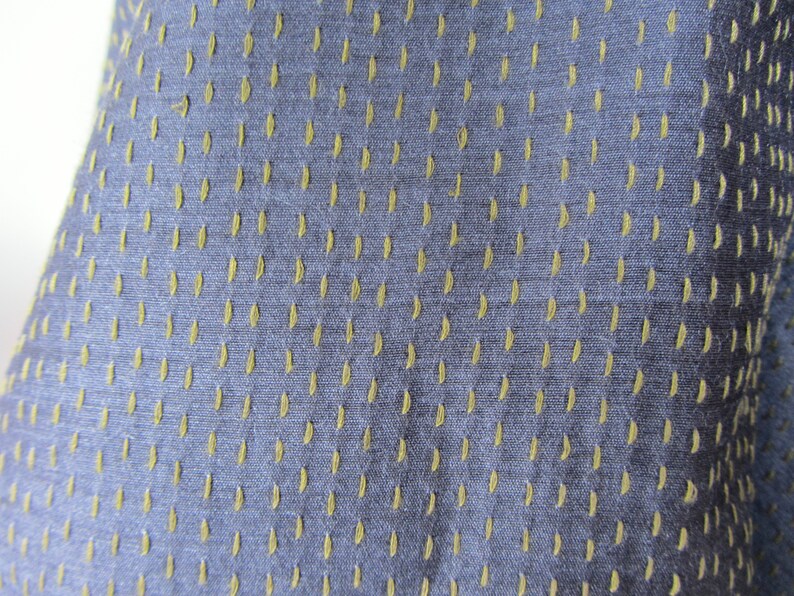 Peut inclure: Gros plan sur un tissu bleu avec un motif subtil de petits points vert clair. Le tissu a une apparence textur&eacute;e et tiss&eacute;e.