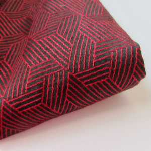 Pode incluir: Tecido vermelho com um padrão geométrico preto. O padrão é feito de linhas finas que criam uma série de quadrados e retângulos.