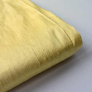 Könnte beinhalten: Nahaufnahme eines blassgelben Stoffes mit einer dezenten, gewebten Textur. Der Stoff ist gefaltet und die Kanten sind sichtbar.