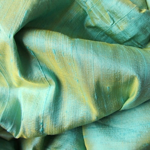 Puede incluir: Primer plano de una tela suave y verde con un brillo sutil. La tela tiene una textura tejida y una apariencia ligeramente arrugada.