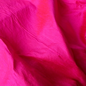 May include: Close-up of a vibrant pink fabric with a subtle sheen. The fabric is wrinkled and has a soft, flowing texture.