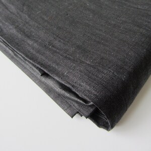 May include: Black fabric folded in a corner. The fabric has a woven texture.