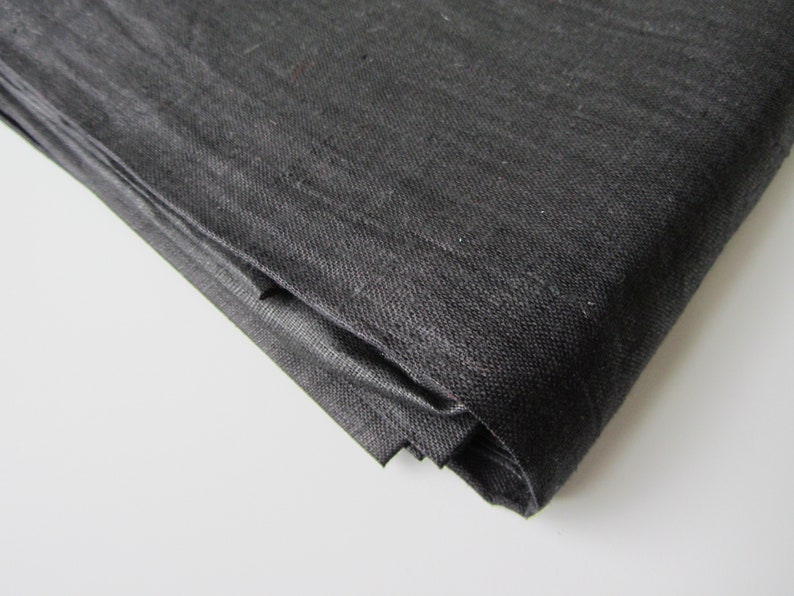 May include: Black fabric folded in a corner. The fabric has a woven texture.