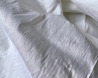 Könnte beinhalten: Weißer Seidenstoff mit einem dezenten, strukturierten, gewebten Muster. Der Stoff ist gefaltet und drapiert und zeigt die weiche, fließende Textur.