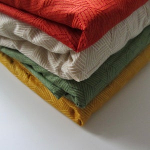May include: A stack of four fabric swatches in different colors and patterns. The top swatch is red with a geometric pattern, the second is beige with a subtle pattern, the third is green with a chevron pattern, and the bottom swatch is yellow with a herringbone pattern.