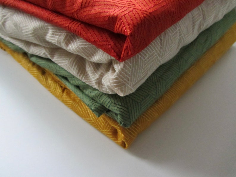 May include: A stack of four fabric swatches in different colors and patterns. The top swatch is red with a geometric pattern, the second is beige with a subtle pattern, the third is green with a chevron pattern, and the bottom swatch is yellow with a herringbone pattern.