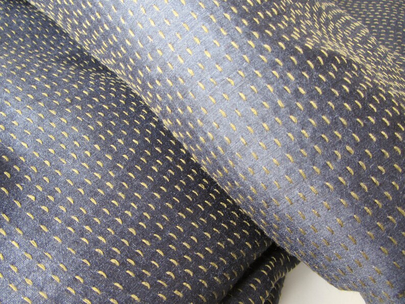 Peut inclure: Gros plan sur un tissu bleu fonc&eacute; avec un motif subtil de surpiq&ucirc;res jaunes. Le tissu a une texture douce.