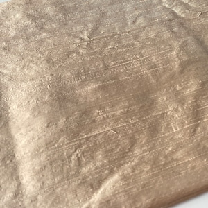May include: A close-up of a piece of fabric with a subtle shimmer. The fabric has a woven texture and a light brown color.