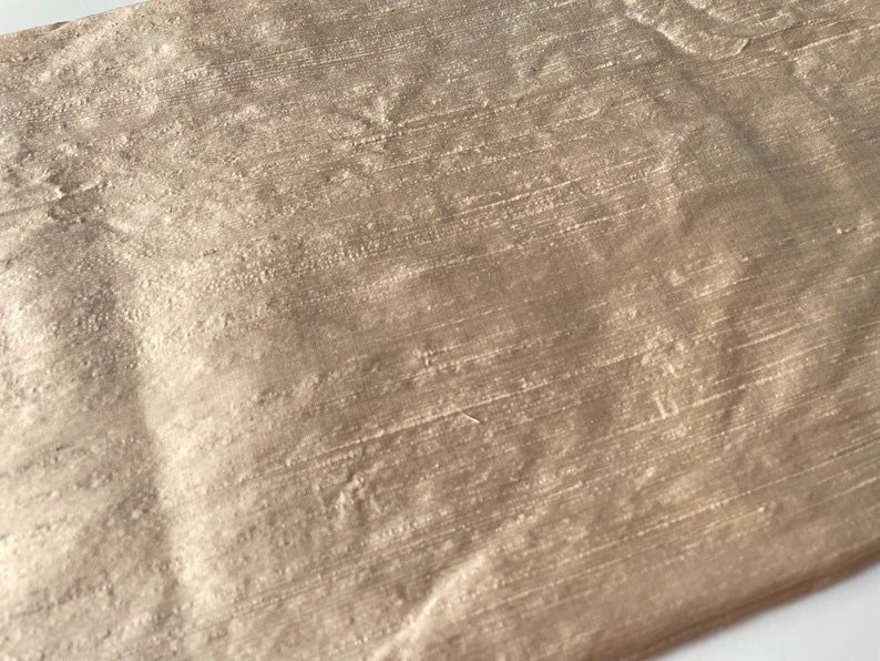 May include: A close-up of a piece of fabric with a subtle shimmer. The fabric has a woven texture and a light brown color.