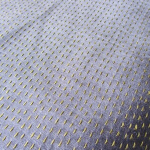 Peut inclure: Gros plan sur un tissu bleu avec un motif subtil de petites coutures dor&eacute;es. Le tissu a une apparence textur&eacute;e et tiss&eacute;e.