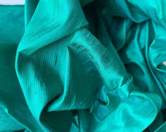 May include: A close-up of a teal green fabric with a smooth, silky texture. The fabric is folded and draped, creating soft folds and curves.