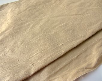 Könnte beinhalten: Nahaufnahme eines beigefarbenen Stoffes mit einem dezenten, strukturierten, gewebten Muster. Der Stoff ist in der Mitte gefaltet und zeigt die glatte, seidenweiche Textur.