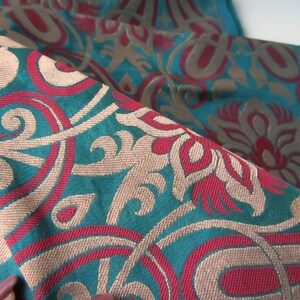 K&ouml;nnte beinhalten: Tealfarbener Stoff mit einem gewebten Muster aus roten, beigefarbenen und wei&szlig;en Blumenmotiven.