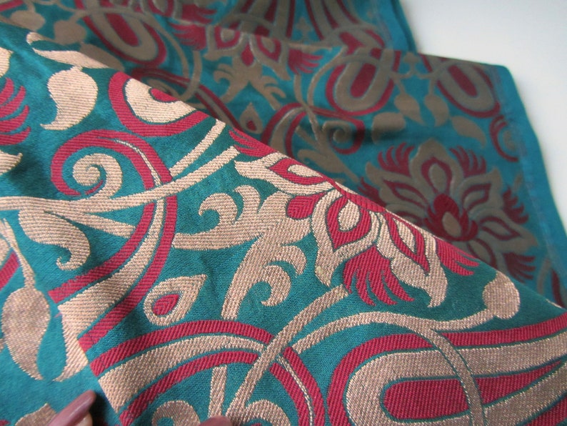 K&ouml;nnte beinhalten: Tealfarbener Stoff mit einem gewebten Muster aus roten, beigefarbenen und wei&szlig;en Blumenmotiven.