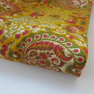 Puede incluir: Primer plano de una tela dorada con un patrón de paisley. La tela tiene un diseño floral rosa y verde.