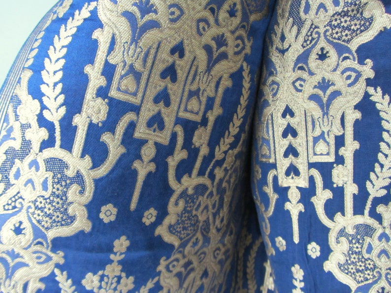 May include: Close-up of a blue fabric with a gold pattern. The pattern features intricate floral designs and repeating heart shapes.