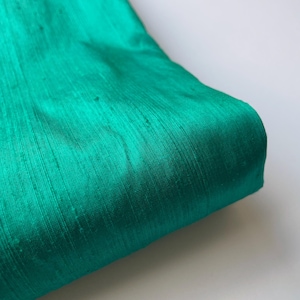 Pode incluir: Close-up de um tecido verde-azulado com um brilho sutil e uma superfície ligeiramente texturizada.