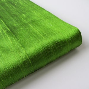 May include: A close-up of a bright green fabric with a subtle sheen. The fabric has a smooth, silky texture and a slightly wrinkled appearance.