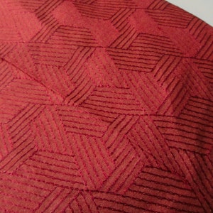 May include: Close-up of a red fabric with a geometric pattern of stitched lines forming a diamond shape.