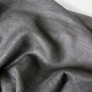 May include: A close-up of a dark gray fabric with a smooth, slightly textured surface. The fabric is folded and draped, showing its soft and flowing nature.